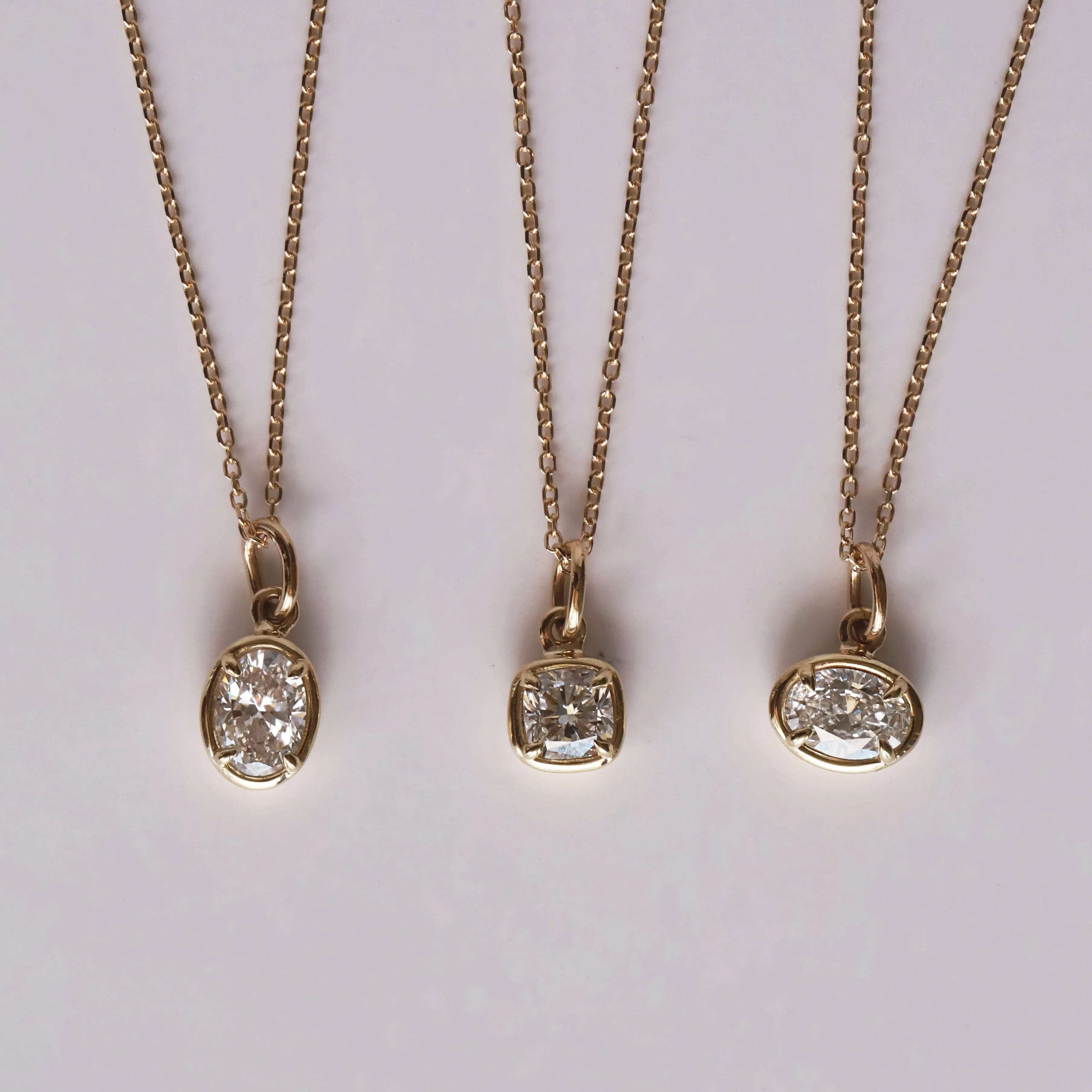 Three gold necklaces with diamond pendants on a light gray background