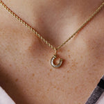 A close-up of a person's neck wearing a delicate gold chain necklace with a small horseshoe-shaped pendant.