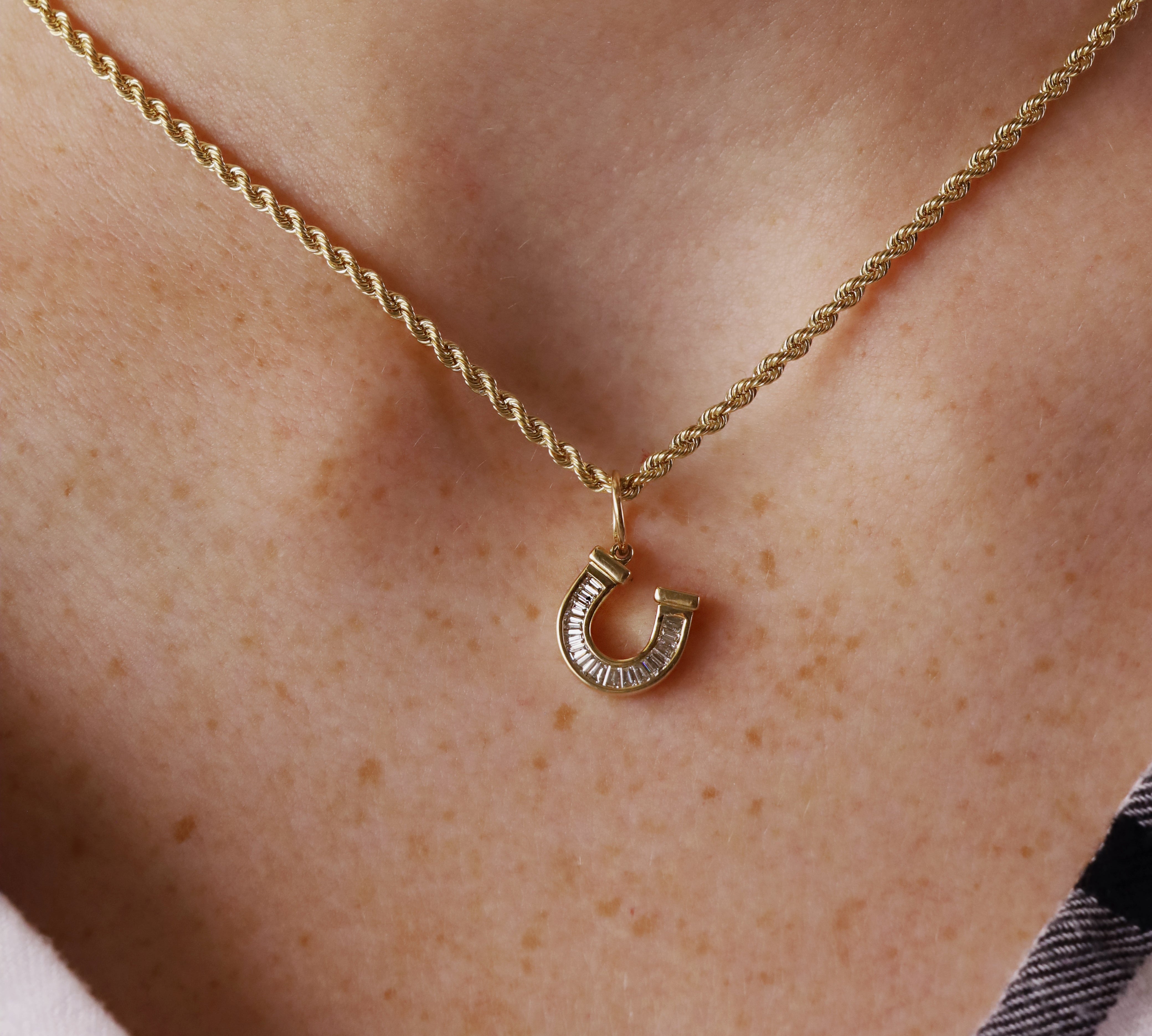 A close-up of a person's neck wearing a delicate gold chain necklace with a small horseshoe-shaped pendant.