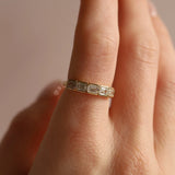 Gold ring with emerald-cut diamonds on a finger against a neutral background