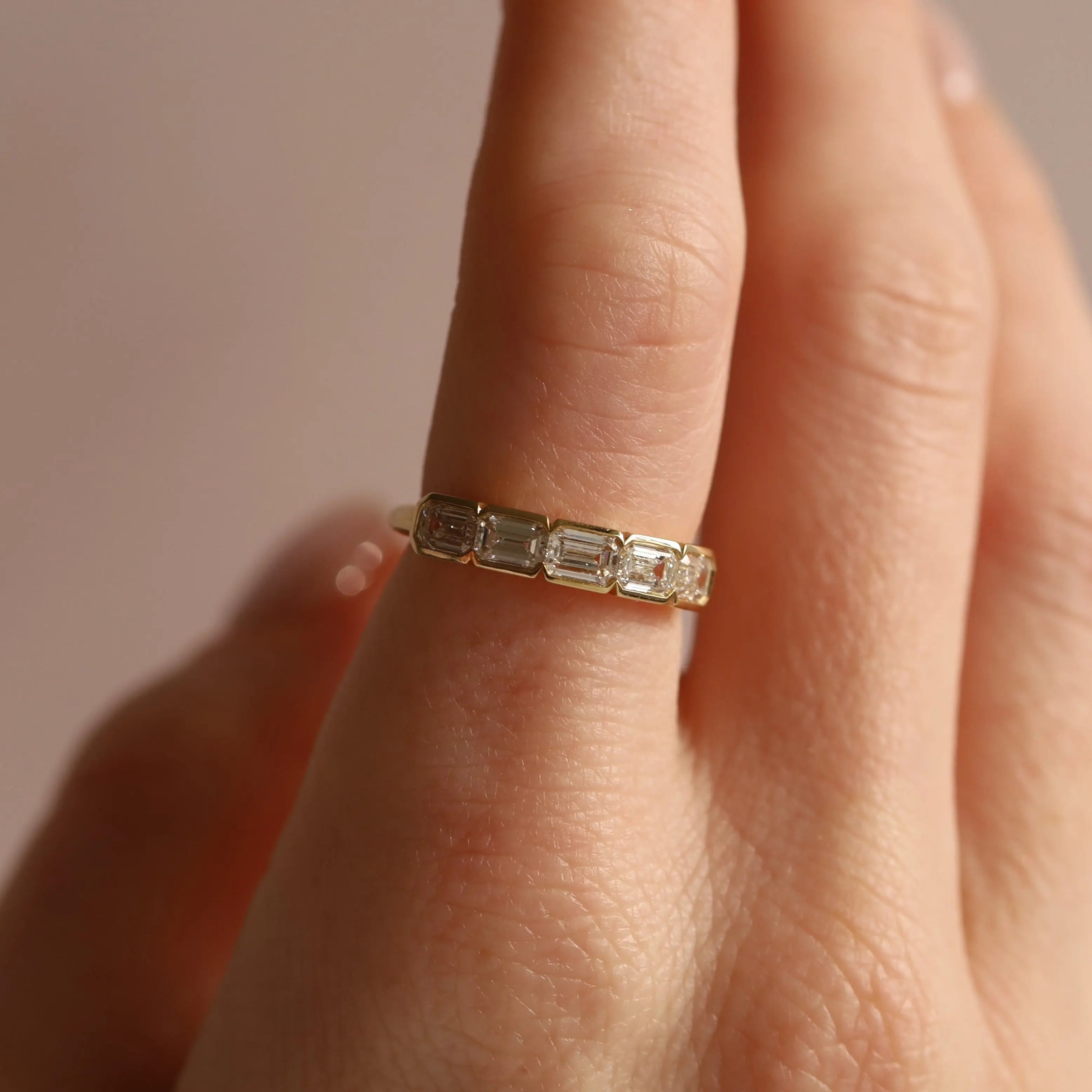 Gold ring with emerald-cut diamonds on a finger against a neutral background