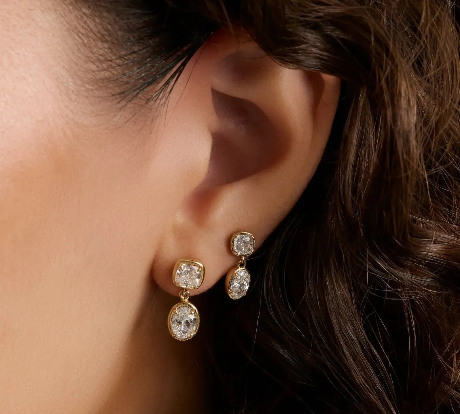 close up of woman's ear with curly hair wearing two drop diamond earrings in yellow gold