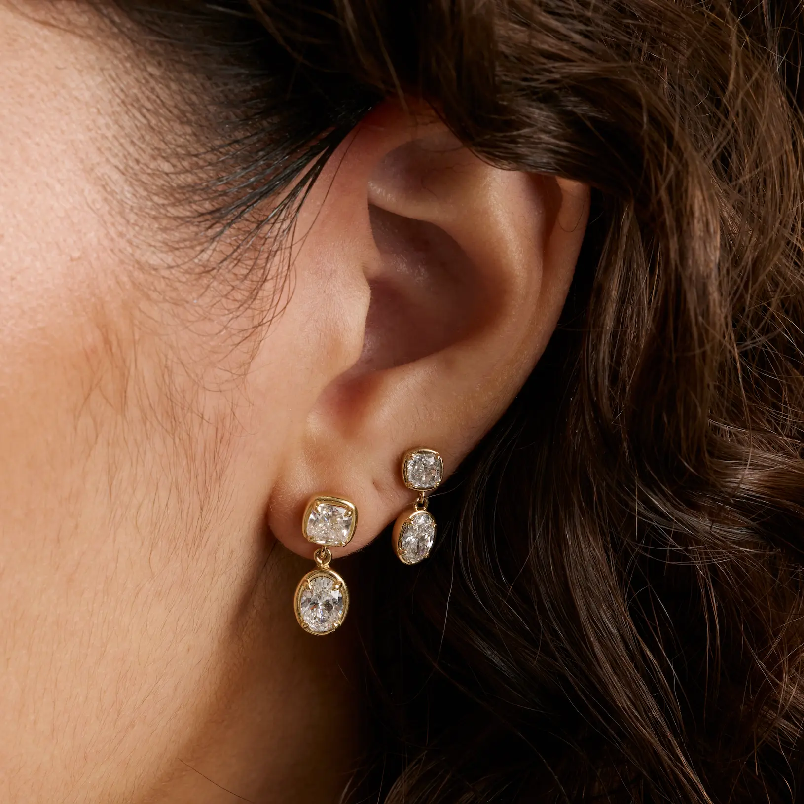 Close up of woman's ear with curly brown hair showing two diamond drop earrings - Large Lisse Dangle Earrings and Lisse Dangle Earrings