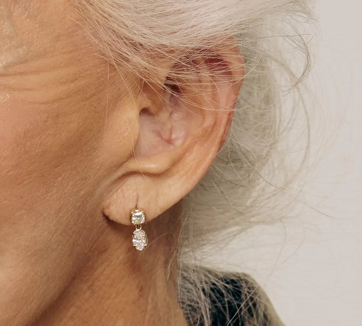 Close-up of an ear wearing a diamond earring with a neutral background