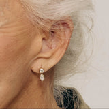 Close-up of an ear wearing a diamond earring with a neutral background