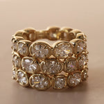 Straight diamond band featuring alternating oval and cushion cut diamonds, set in yellow gold. 3 of them stacked together against a neutral background.