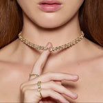 Close-up of a woman wearing a gold necklace and rings on a neutral background