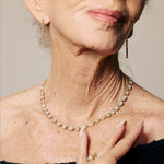 Close-up of a woman wearing a diamond necklace and earrings against a neutral background