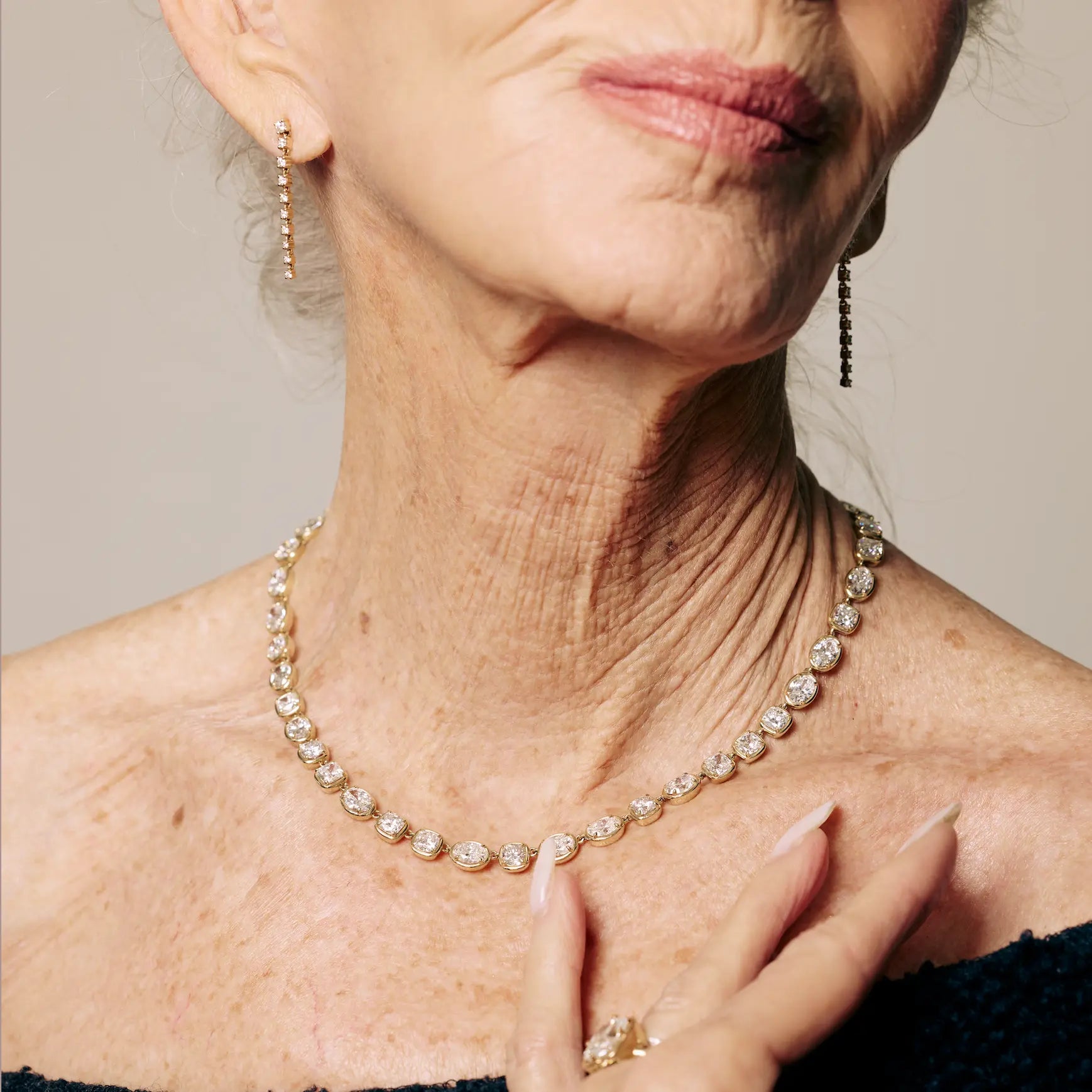 Close-up of a woman wearing a diamond necklace and earrings against a neutral background