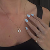 woman's décolletage with yellow gold paperclip chain and yellow gold and diamond horseshoe charm against a dark background