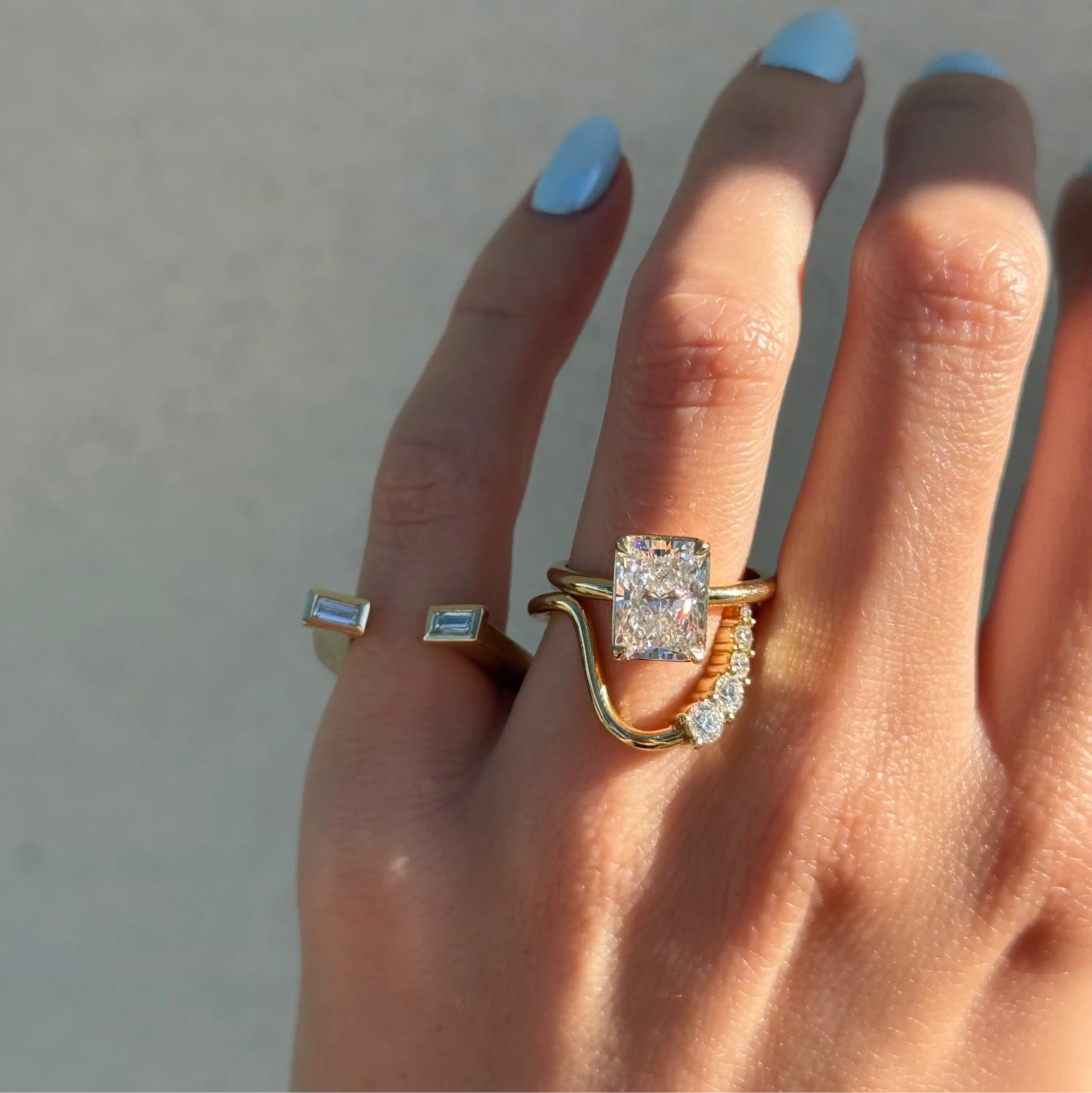 close up of hand against a neutral background, wearing yellow gold and diamond rings