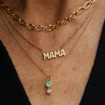 Gold 'MAMA' necklace with a small pendant on a person's neck against a black background