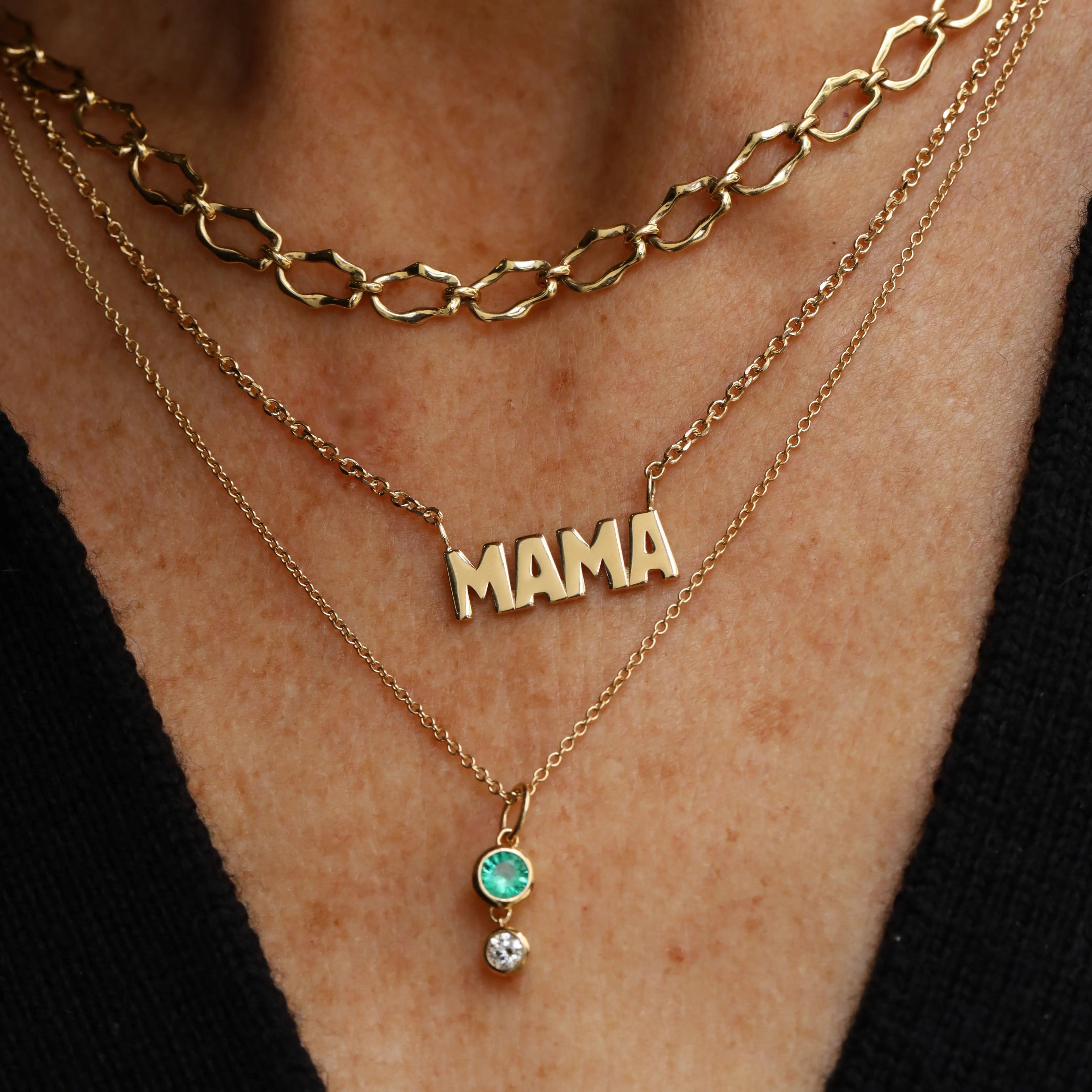 Gold 'MAMA' necklace with a small pendant on a person's neck against a black background