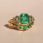 Gold ring with emerald green gemstones on a beige background
