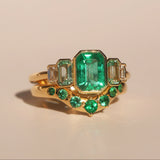 Gold ring with emerald green gemstones on a beige background