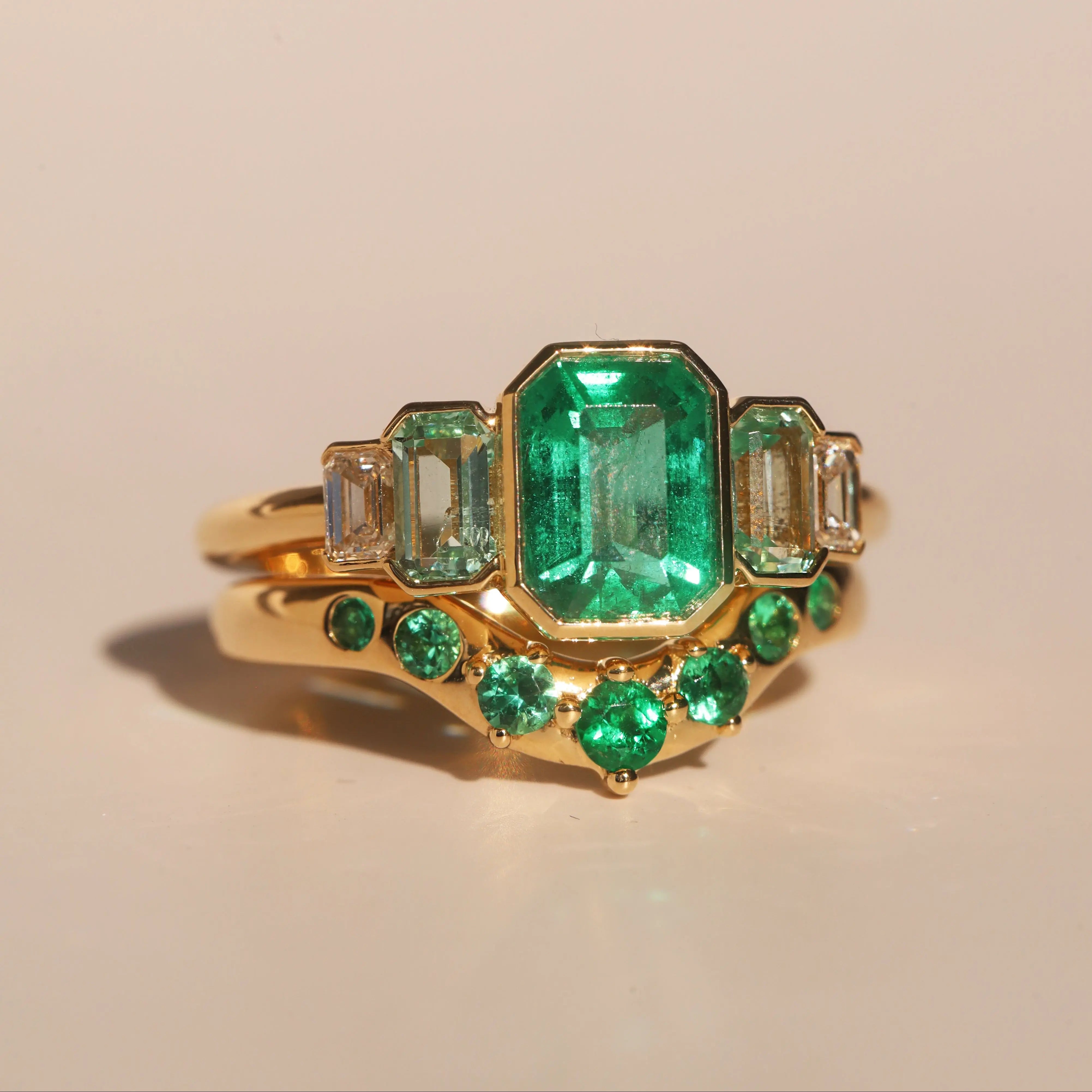 Gold ring with emerald green gemstones on a beige background