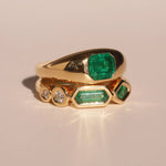 Gold rings with emerald and diamond stones on a beige background