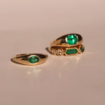 Two gold rings with emerald stones on a beige background