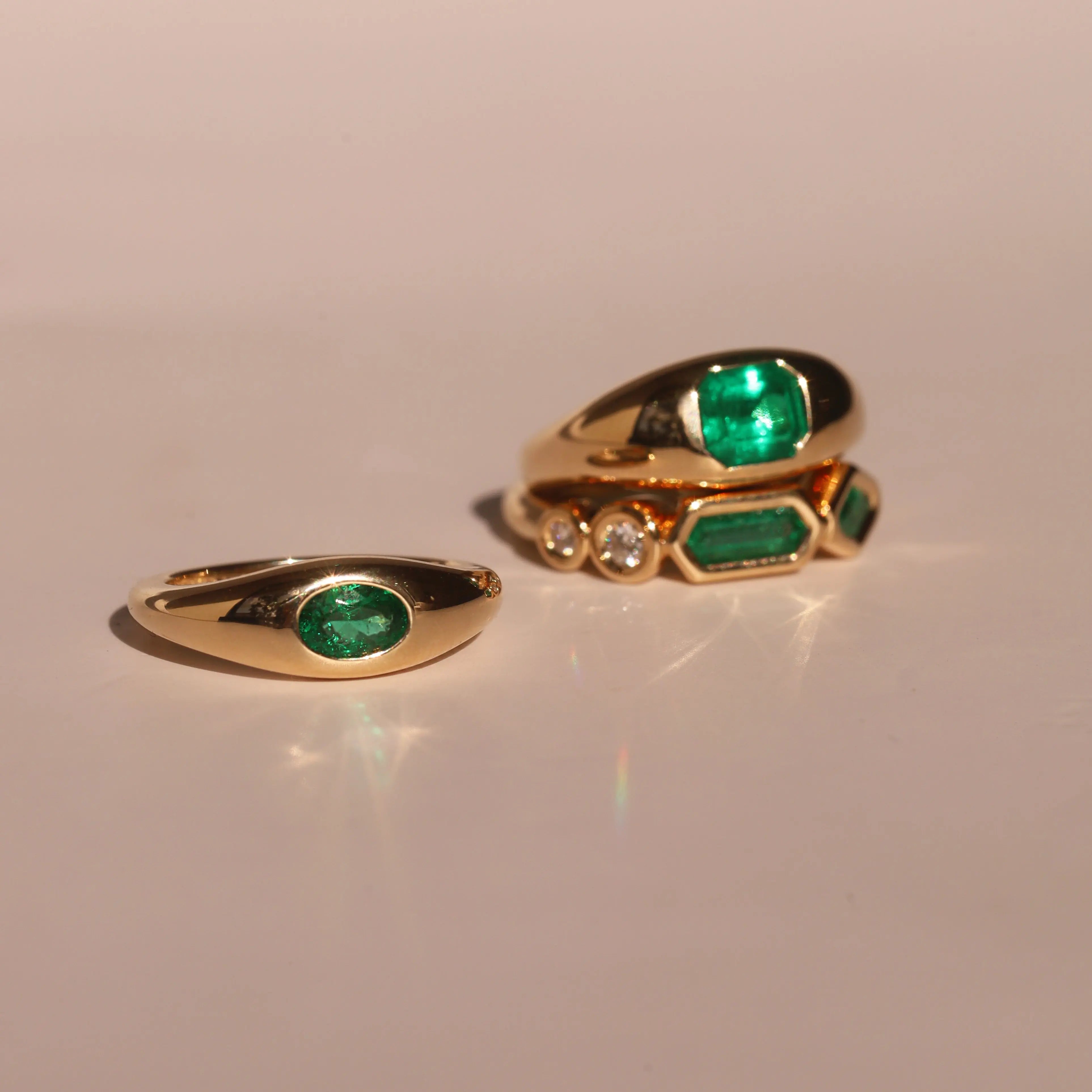 Two gold rings with emerald stones on a beige background