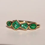 Gold ring with emerald green gemstones on a beige background
