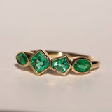 Gold ring with emerald green gemstones on a beige background