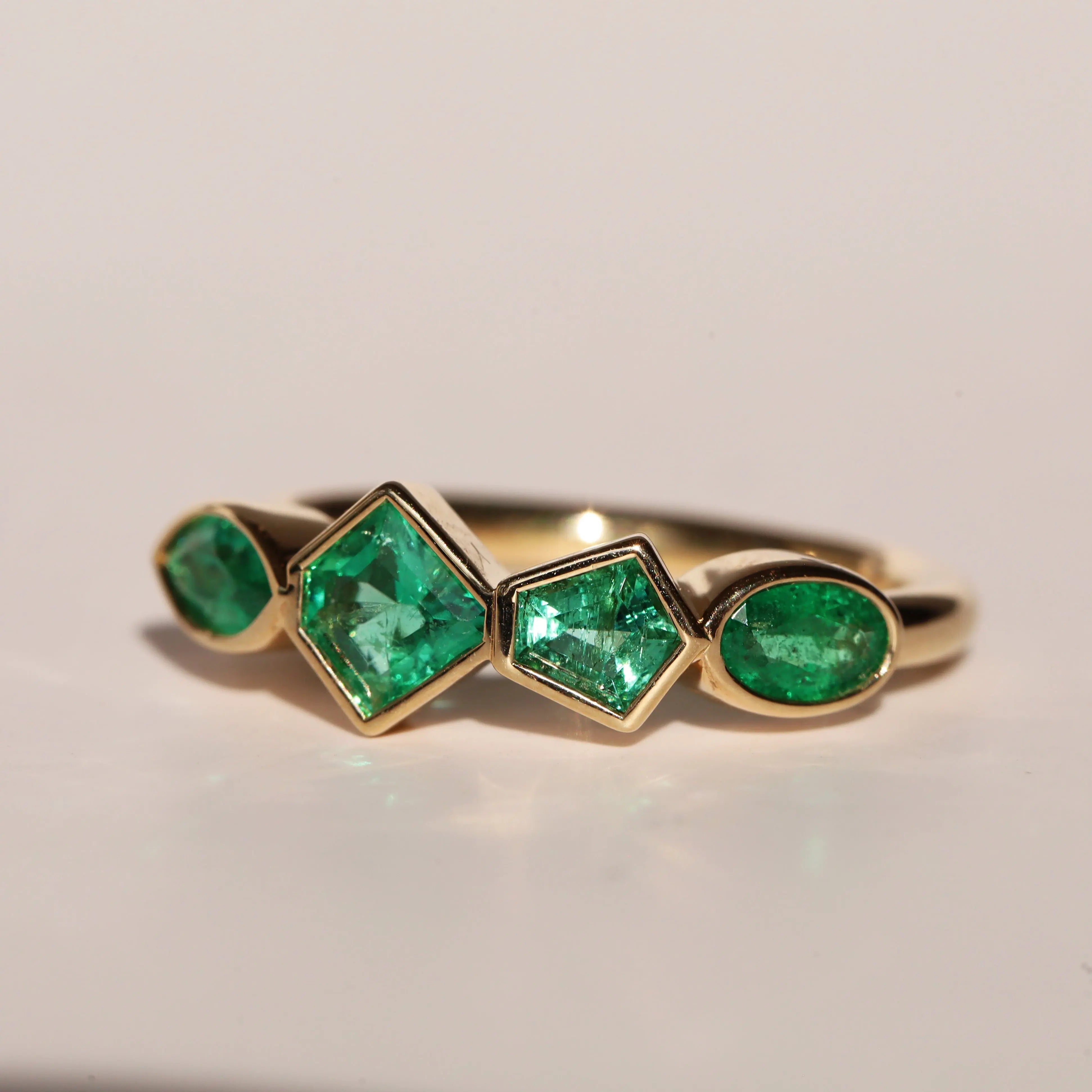 Gold ring with emerald green gemstones on a beige background