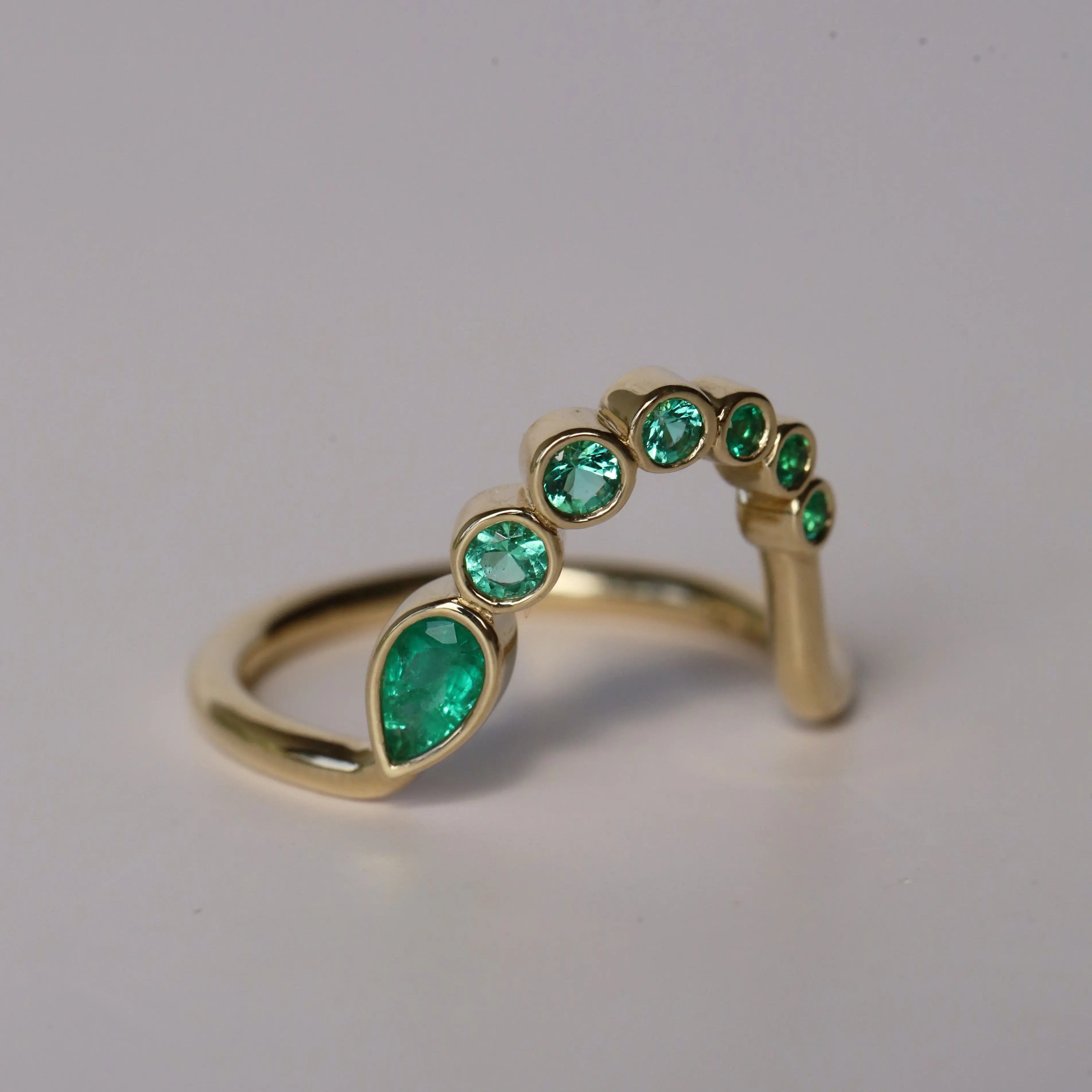 Gold ring with green gemstones on a gray background