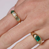 Gold ring with emerald stones on a finger against a white background