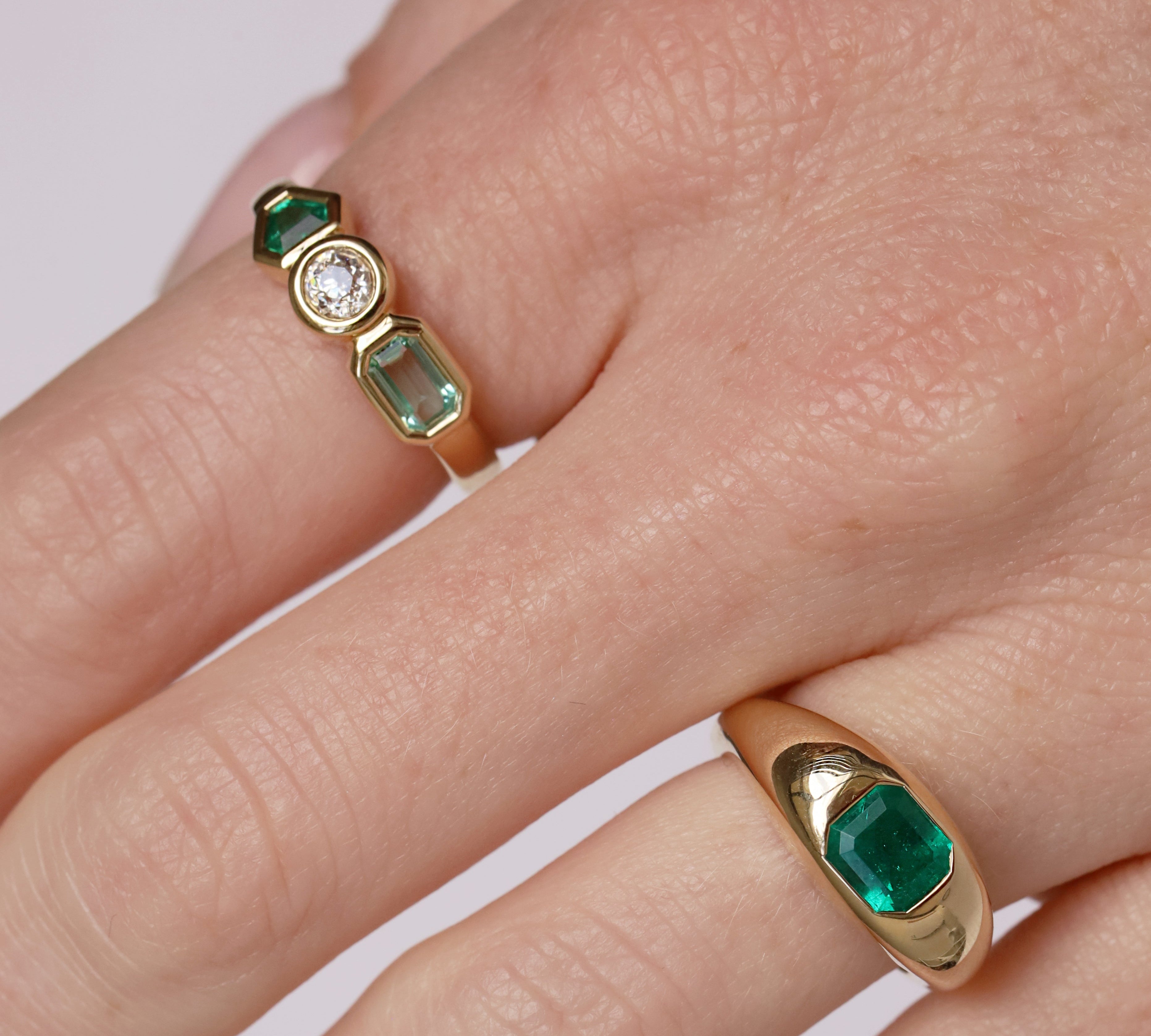 Gold ring with emerald stones on a finger against a white background