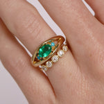 Gold ring with emerald and diamonds on a finger against a white background