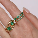 Gold and emerald ring on a finger against a white background