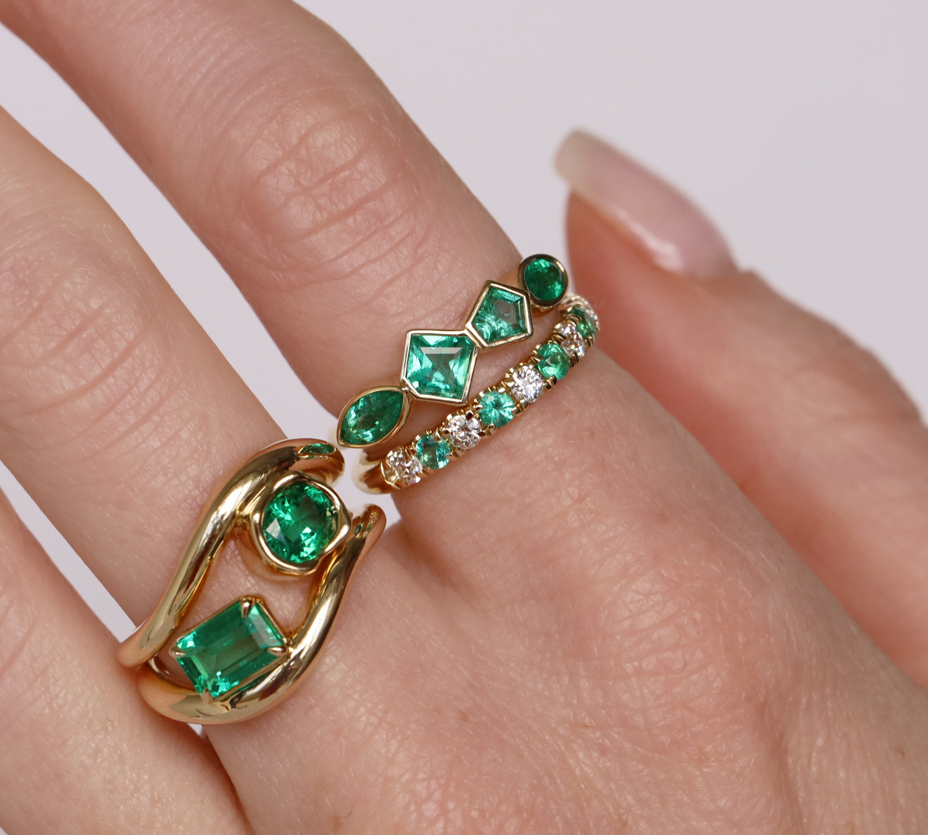 Gold and emerald ring on a finger against a white background