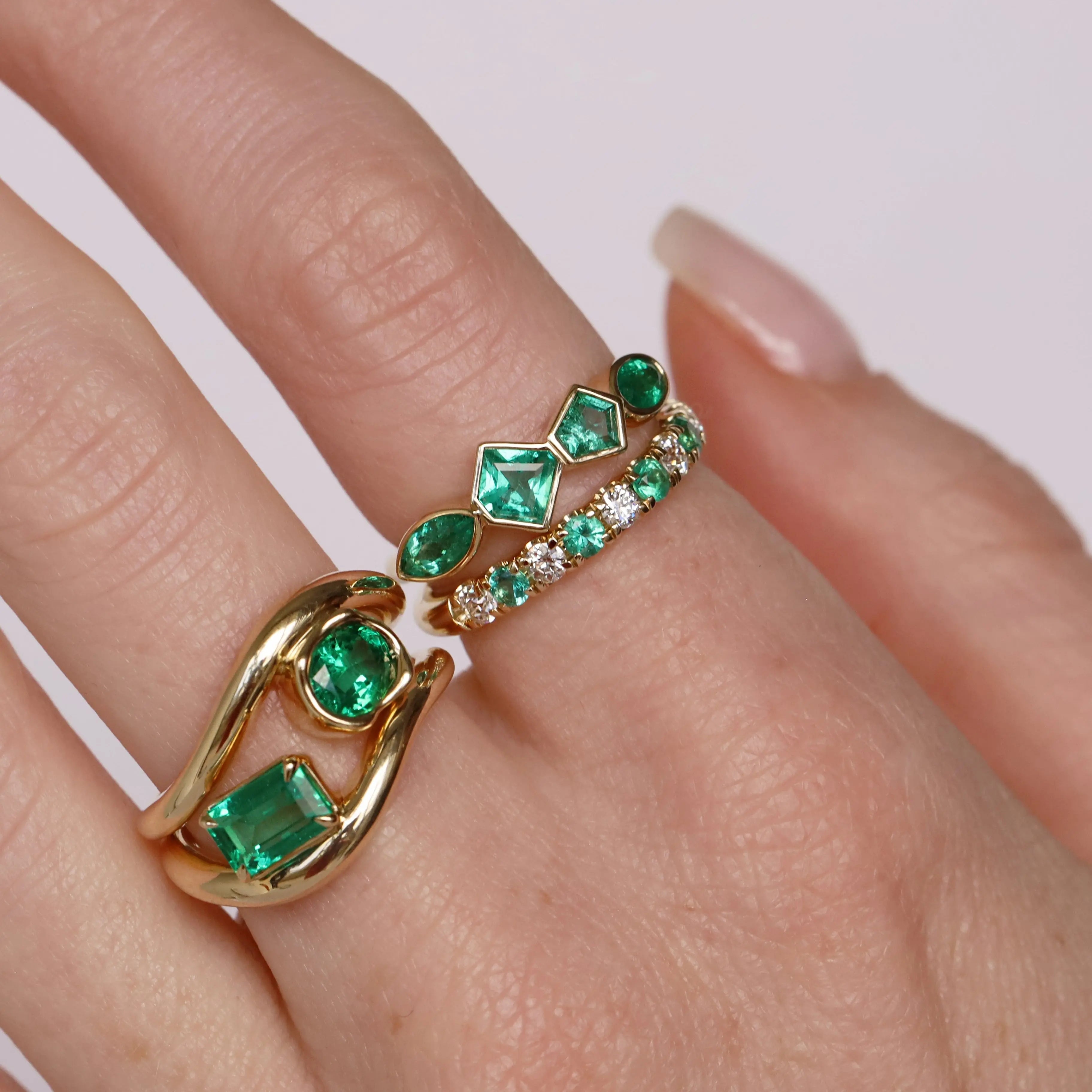 Gold and emerald ring on a finger against a white background