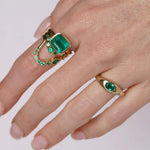 Gold rings with emerald stones on a hand against a white background