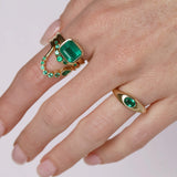 Gold rings with emerald stones on a hand against a white background