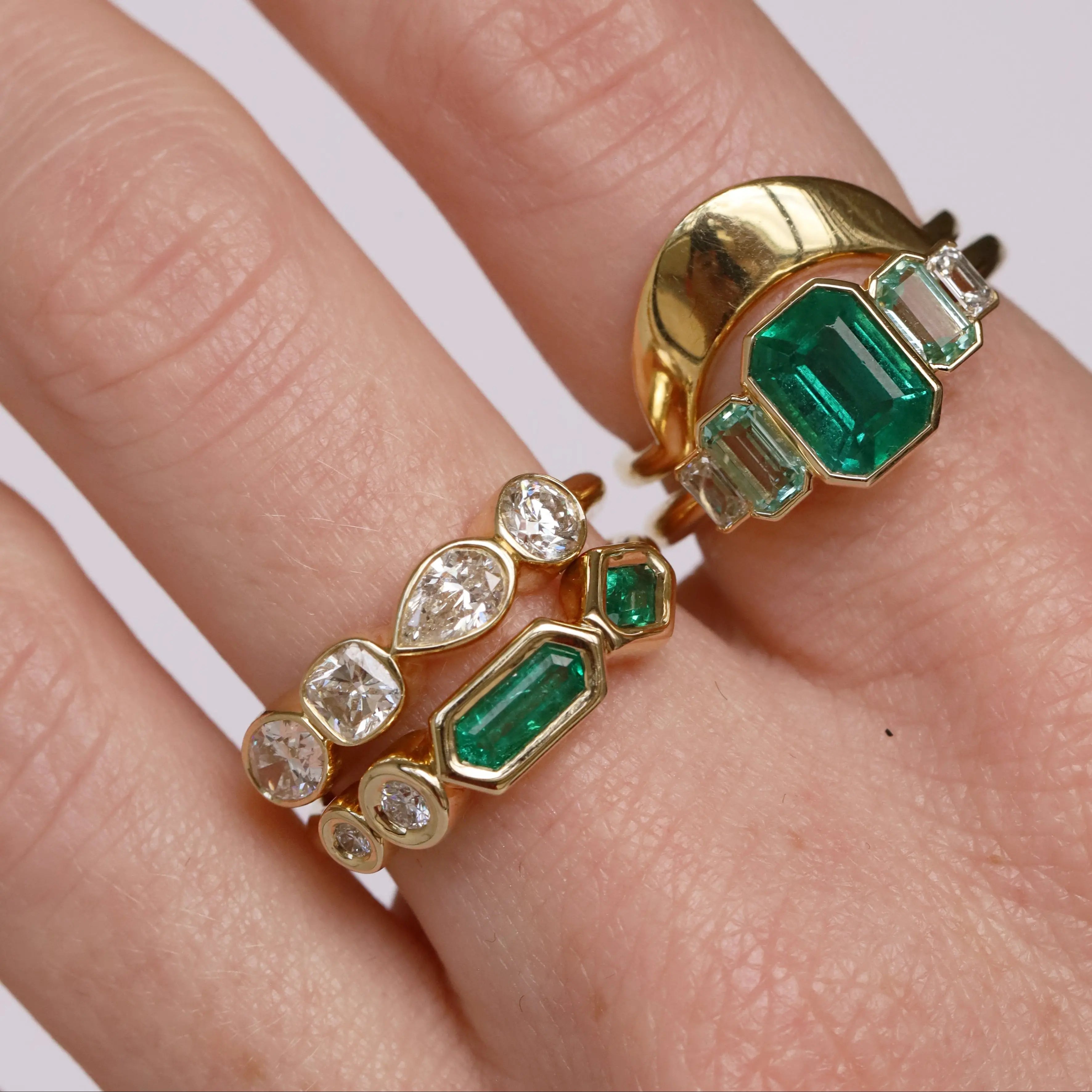 diamond and emerald rings on woman's hand, against white background
