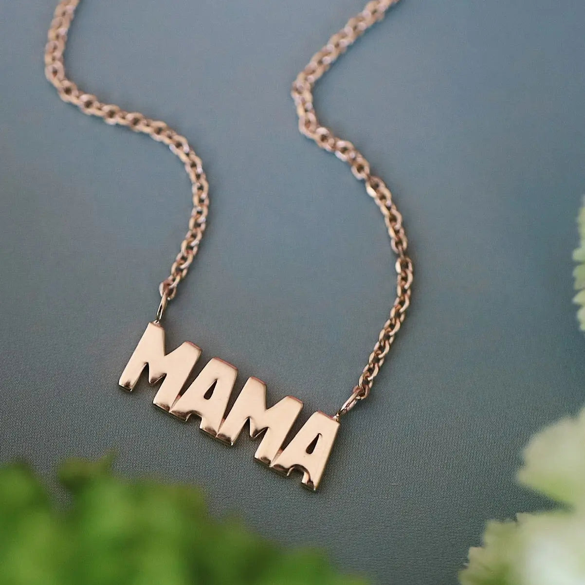 Yellow gold 'MAMA' necklace on a green background