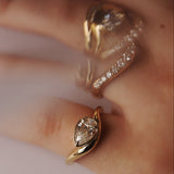 Gold rings with diamonds stacked on a hand up close, with slightly blurry effect against a neutral background 