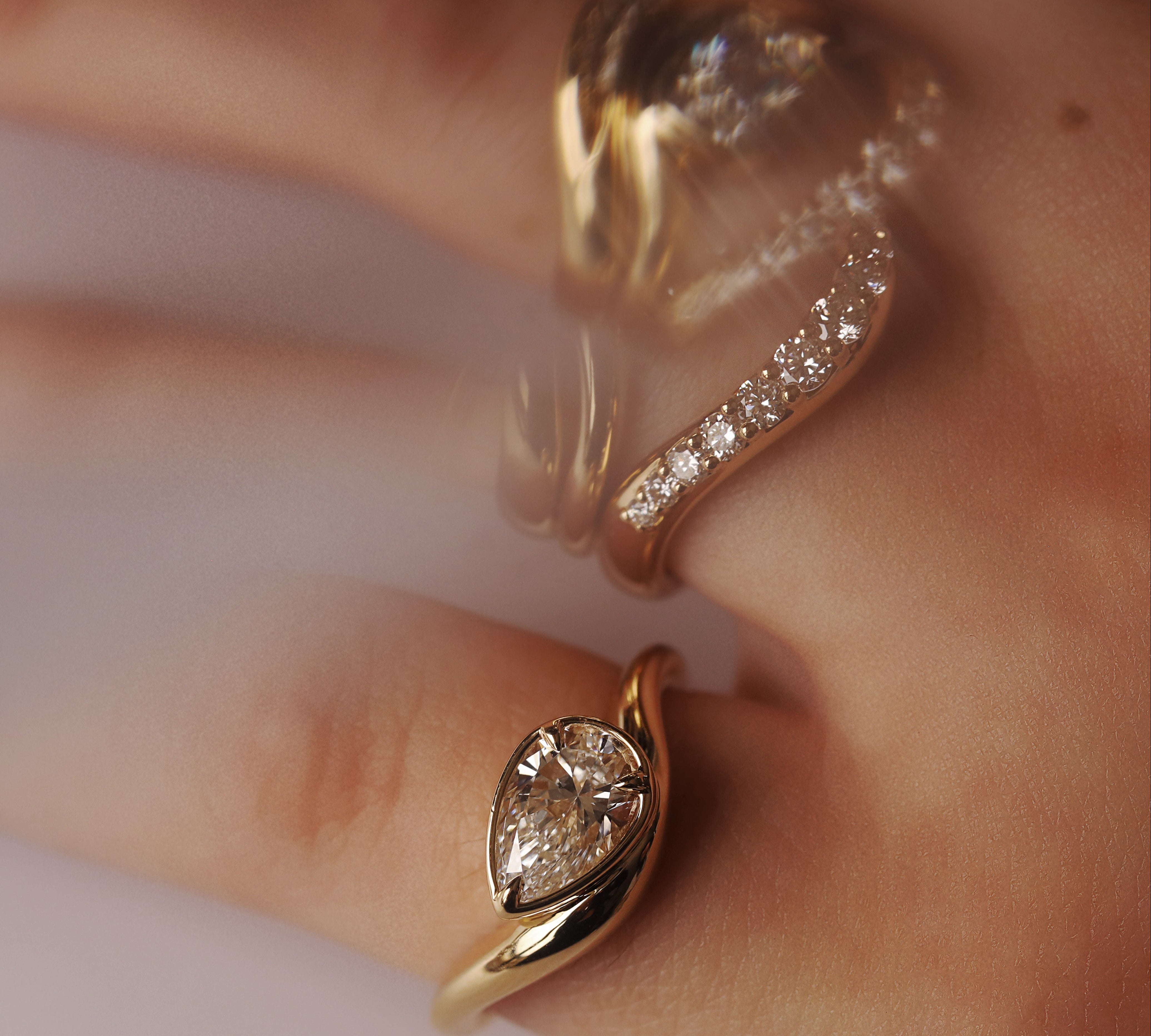 Gold rings with diamonds stacked on a hand up close, with slightly blurry effect against a neutral background 