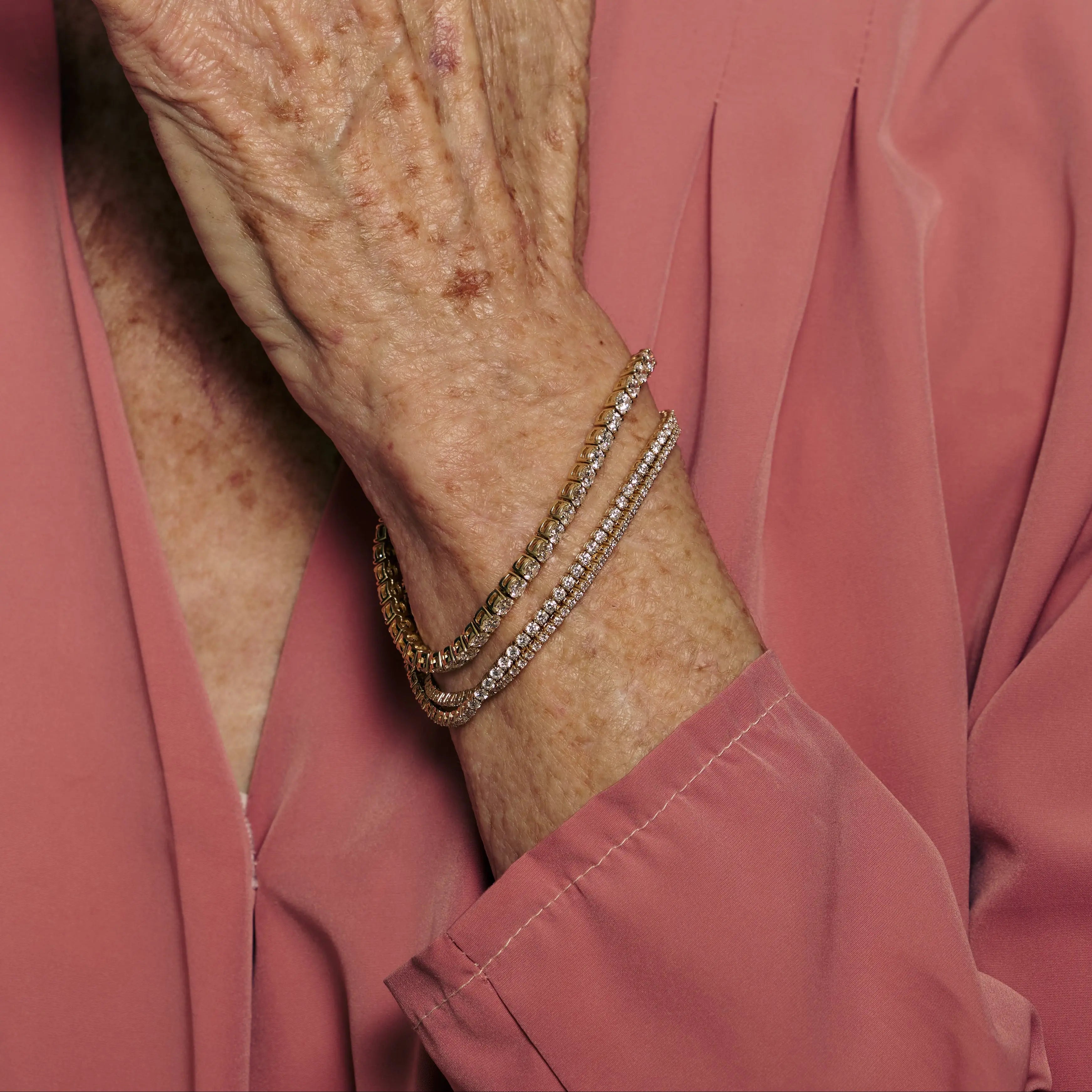 Close-up of an elderly person's arm wearing a bracelet with a pink shirt background