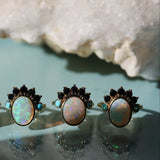 Four pairs of opal earrings with black and gold accents on a light blue background.