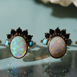 Pair of opal rings with black and blue gemstones on a reflective surface.