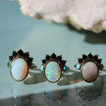Four pairs of opal earrings with black and gold accents on a light blue background.