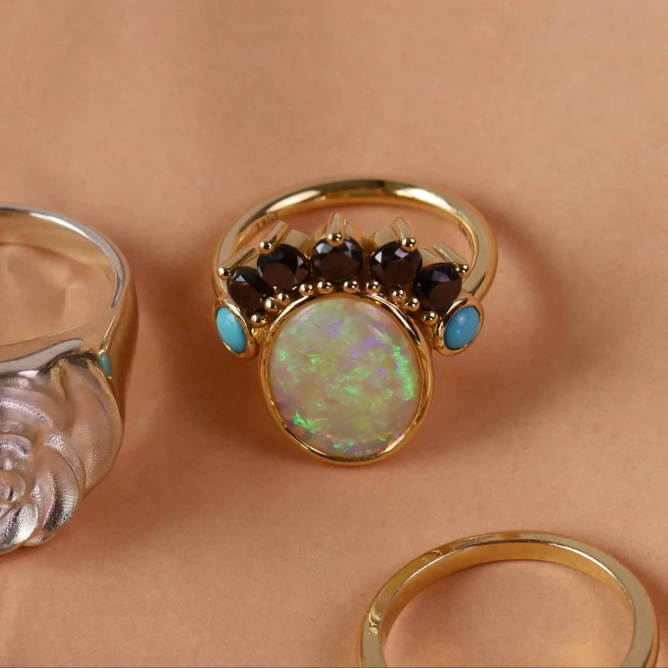 Photo of three rings on an orange background, featuring a gold opal ring with black diamond and turquoise accent stones.