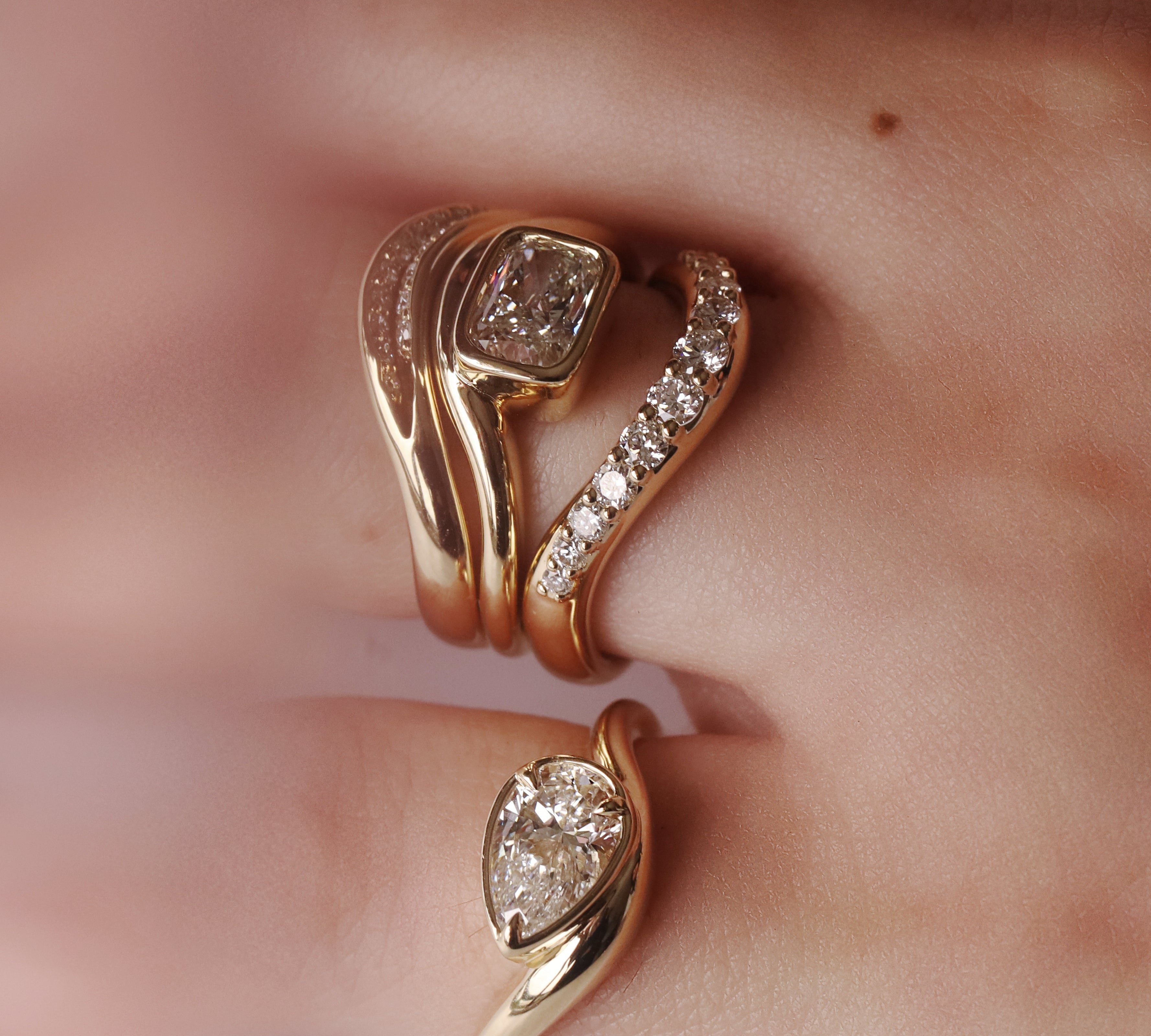 Close up of hand with multiple yellow gold and diamond rings styled together