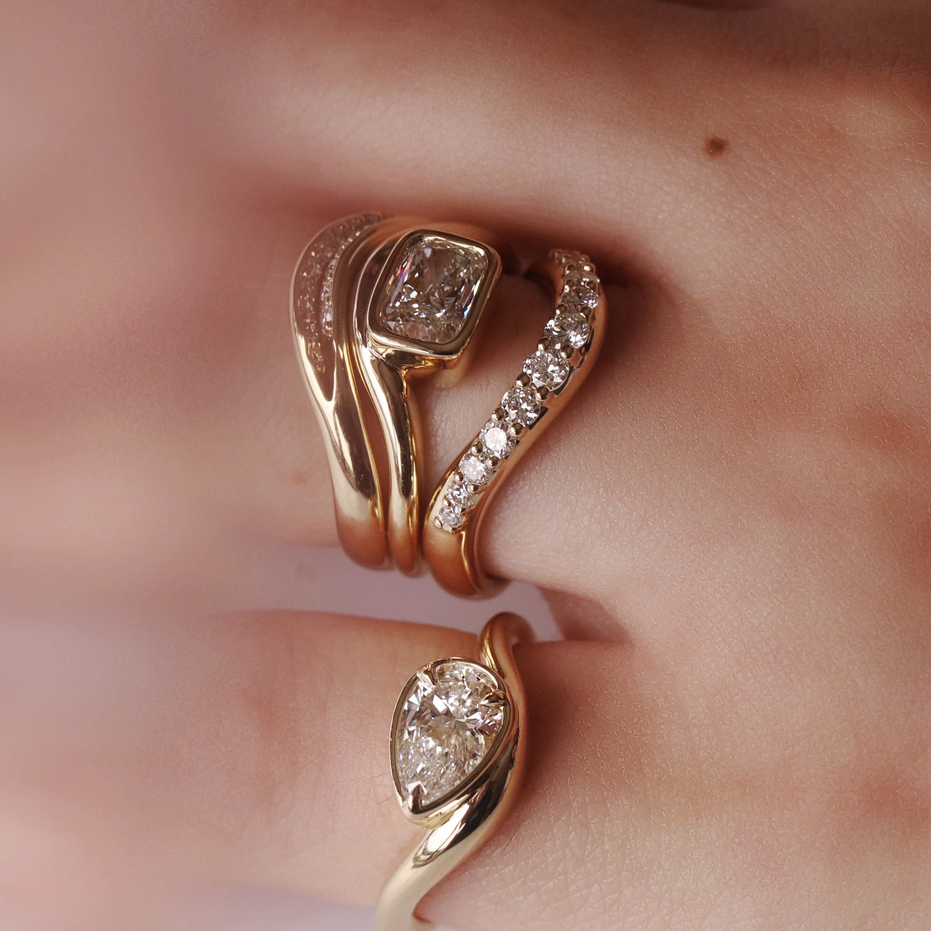 Close up of hand with multiple yellow gold and diamond rings styled together
