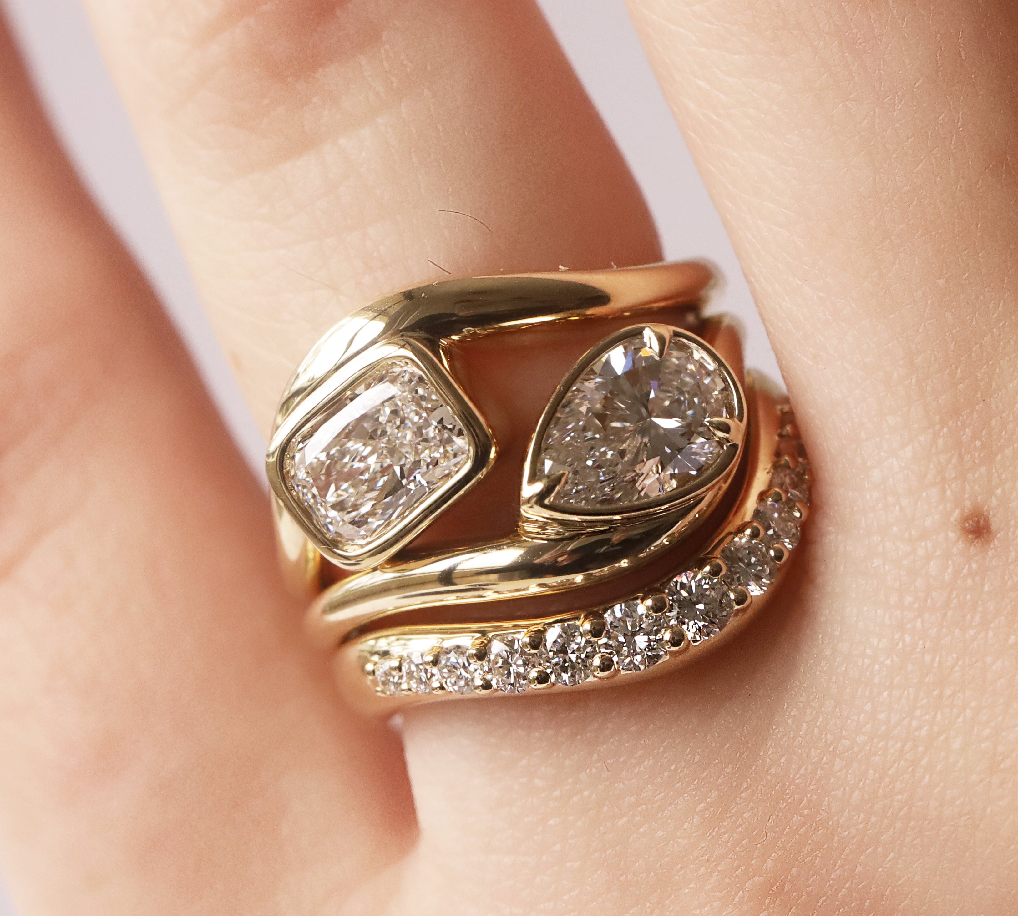Gold ring with diamonds on a finger against a neutral background