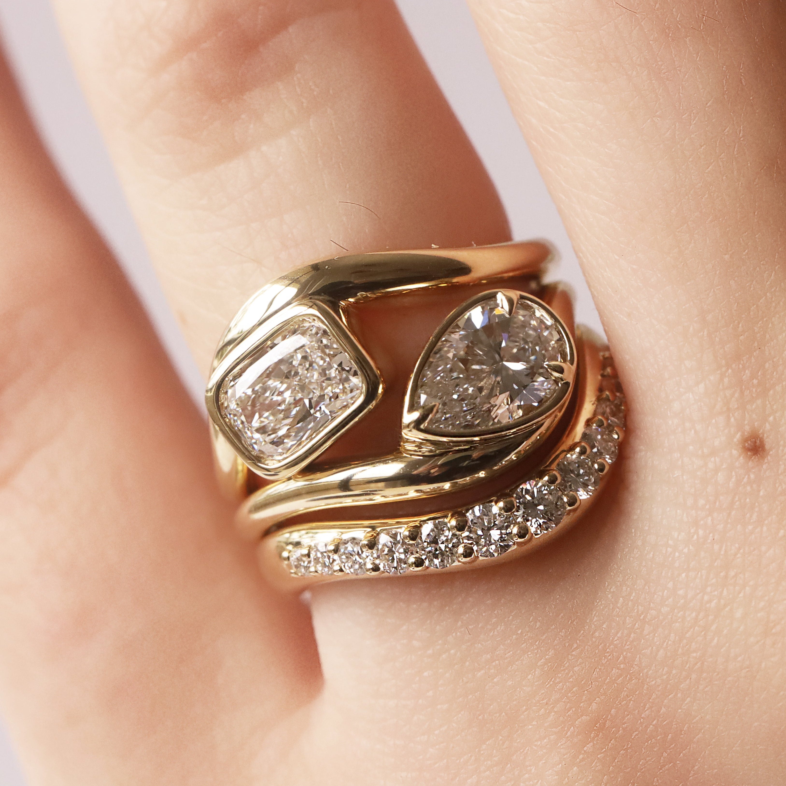 Gold ring with diamonds on a finger against a neutral background