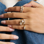A close-up of a hand wearing multiple gold rings with clear gemstones, resting on blue denim fabric.