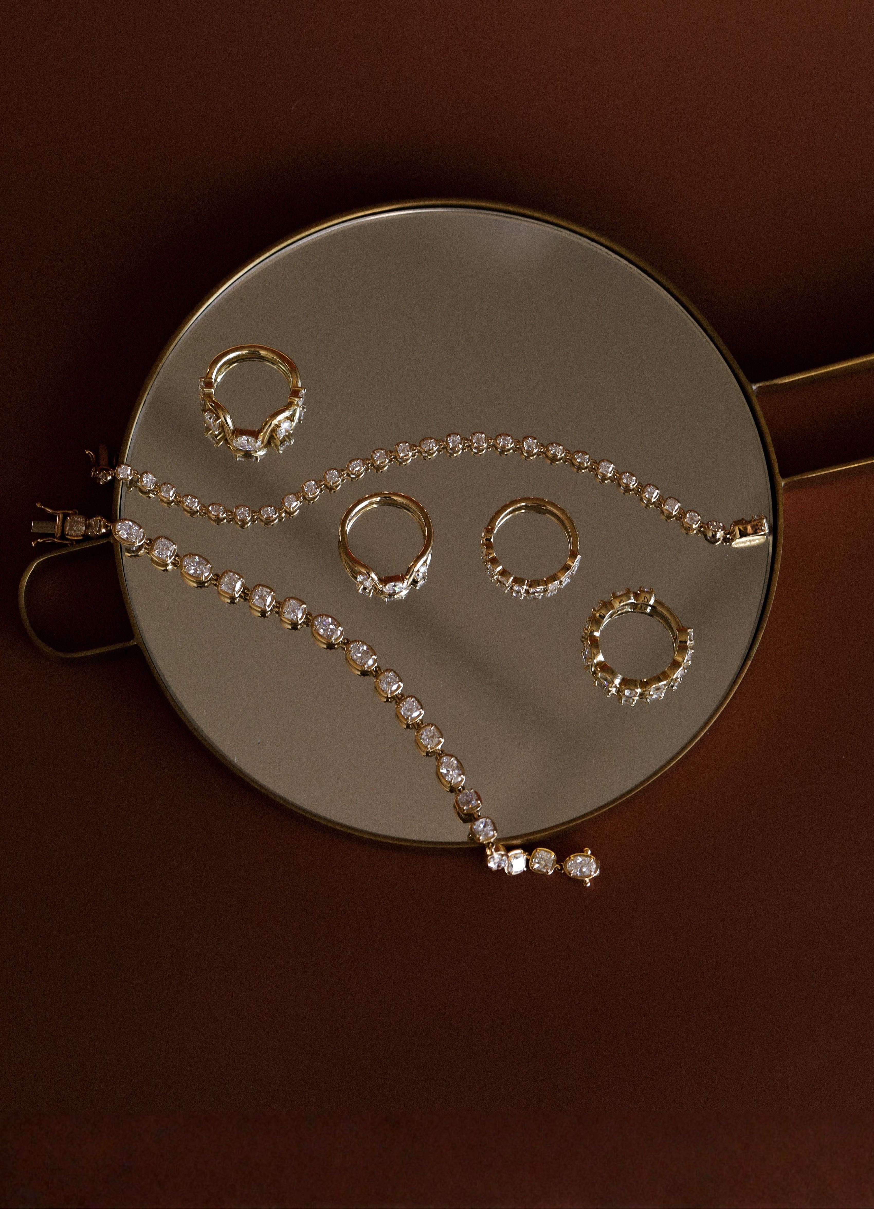 Set of rings and diamond bracelets on a round mirror with a brown background